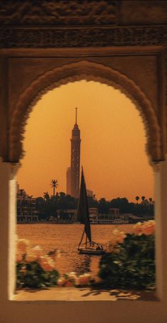 a sailboat in the water under an arch with a clock tower in the background