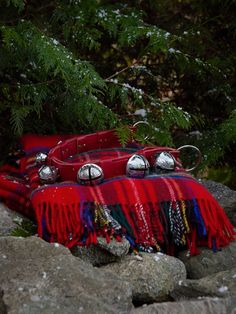 two red purses with bells on them sitting on some rocks near trees and snow