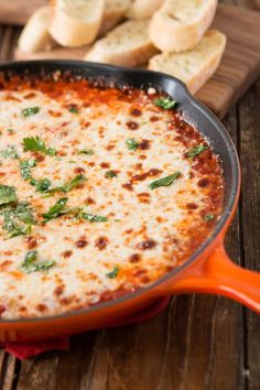 a close up of a pizza in a pan on a wooden table next to bread