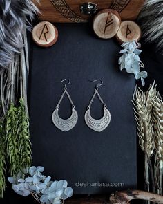 two pairs of earrings sitting on top of a black board next to some dried flowers