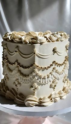 a three layer cake with white frosting and gold decorations on it's side