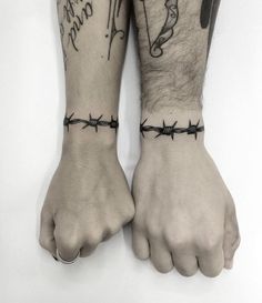 two men's hands with barbed wire tattoos on their arms and wristbands