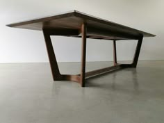 a wooden table sitting on top of a cement floor next to a white wall in an empty room