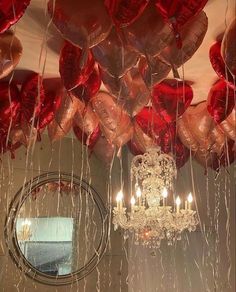 a chandelier hanging from the ceiling filled with red heart shaped balloons