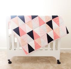 a baby crib with a pink, black and white quilt on the top of it