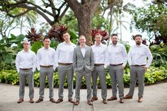 a group of men standing next to each other wearing white shirts and gray pants with brown shoes