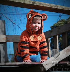 a little boy wearing a tiger costume on top of a wooden deck with a fence in the background