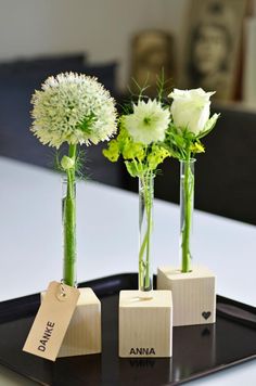 three vases with flowers are sitting on a tray that has tags attached to them