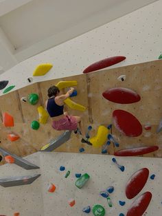 a man climbing up the side of a rock wall with colorful rocks and plastic tools