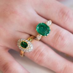 a woman's hand holding two rings with emeralds and diamonds