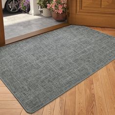 a door mat is on the floor in front of a doorway with flowers and potted plants