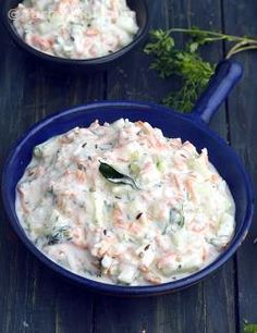 two blue bowls filled with coleslaw on top of a wooden table and garnished with parsley