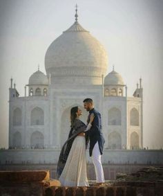 a man and woman standing in front of a white building with a large dome on top