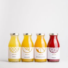 four bottles of juice are lined up on a white surface, each containing different flavors