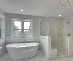 a large white bathtub sitting next to a window in a bathroom under a chandelier