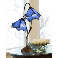 a table with a vase and two blue glass flowers on it next to a window