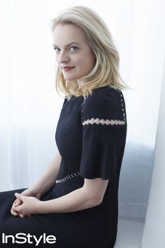 a woman sitting in front of a window wearing a black dress