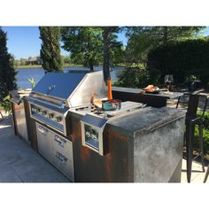 an outdoor bbq with grill and chairs next to water