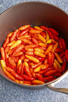 a pan filled with red and yellow peppers on top of a blue countertop next to a wooden spoon