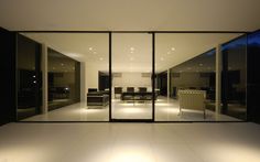 an empty room with large glass doors leading into the living room and dining area at night