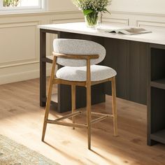 a white counter top sitting under a window next to a wooden bar stool with a flower vase on it