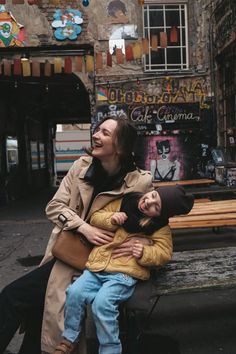 a woman sitting on top of a bench next to a man holding a small child