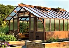 there is a small wooden greenhouse in the middle of some plants and flowers around it