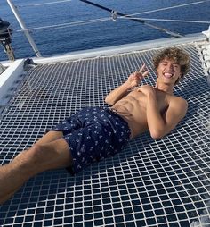 a young man laying on the deck of a sailboat with his hand up in the air