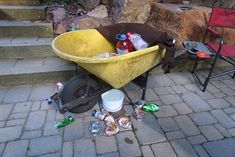 a yellow wheelbarrow filled with trash sitting on top of a brick sidewalk next to stairs