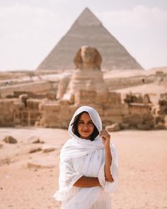 a woman standing in front of the pyramids with her hand on her hip and looking at the camera