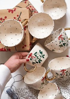 a person is holding a coffee cup in front of many other cups and saucers