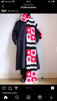 a man standing in front of a white wall wearing a black coat and red and white crocheted scarf