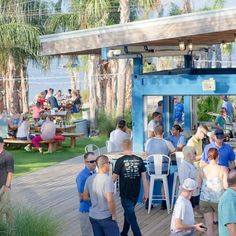 a group of people standing around tables and chairs on a wooden deck near the water