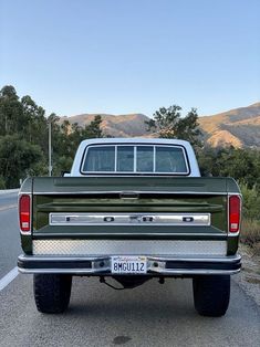 the back end of a green truck parked in a parking lot with mountains in the background