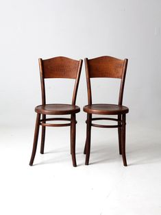 two wooden chairs sitting next to each other on a white surface with one chair facing the other