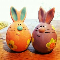 two ceramic easter bunnies sitting on top of a wooden table