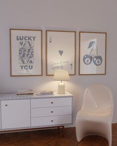 a white chair sitting next to a table with a lamp on it in front of two pictures