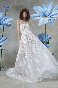 a woman standing in front of blue flowers wearing a white dress with an embellishment on it