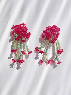 two pink flowers are attached to earrings on a white surface with shadows from the fabric