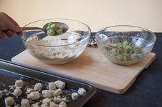 two bowls filled with food sitting on top of a wooden cutting board next to a cookie sheet