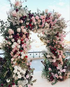 an outdoor wedding ceremony with flowers and greenery on the side of the aisle, overlooking the water