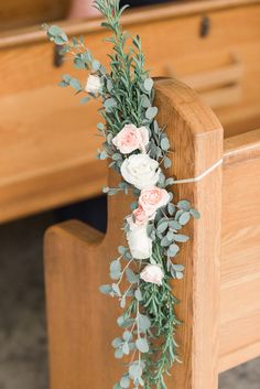 flowers and greenery are tied to the back of a wooden church pew during a wedding ceremony