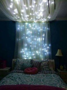 a bed with lights hanging from the ceiling in front of a curtained window over it