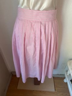 "This gorgeous button down pink and white skirt is so pretty! The composition is 50% polyester and 50% cotton. Would be perfect paired with cowboy boots and a prairie shirt, or with a white blouse tucked in and leather huaraches. Our best guess is that it is a women's medium to large, it is marked a size 11/12. But please check the measurements given below to ensure a proper fit. It was made in the early 1980's in the USA by Avon Fashions, and buttons completely down. It is in good condition wit Spring Striped Flared Skirt, Spring Striped Skirted Bottoms, Spring Relaxed Skirt With Striped Hem, Striped Skirt For Spring Daywear, Relaxed Skirt With Striped Hem For Spring, Striped Pleated Knee-length Skirt, Striped Skirted Bottoms For Spring, Pink Full Skirt Bottoms For Day Out, Spring Striped Pleated Skirt