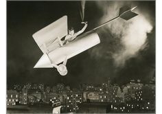 a man flying through the air while riding on top of a glider plane in front of a cityscape