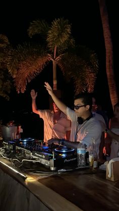 two djs at a party with palm trees in the background