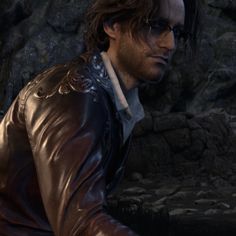 a man with glasses and a leather jacket is standing in front of a rock wall