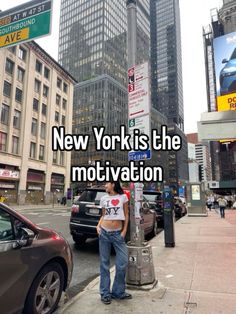 a woman standing on the side of a street next to a pole with a sign that says new york is the motivation