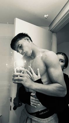 a shirtless man is looking at his reflection in the mirror while another woman stands next to him