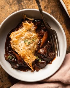 a white bowl filled with food on top of a wooden table next to a fork